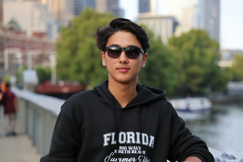 Casual portrait of a young man wearing sunglasses, standing outdoors in a city environment.