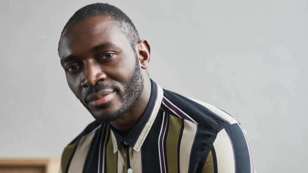 Close-up portrait of a confident man with facial hair, wearing a striped shirt.