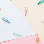 An artistic flat lay featuring colorful hair clips on a pastel geometric background.